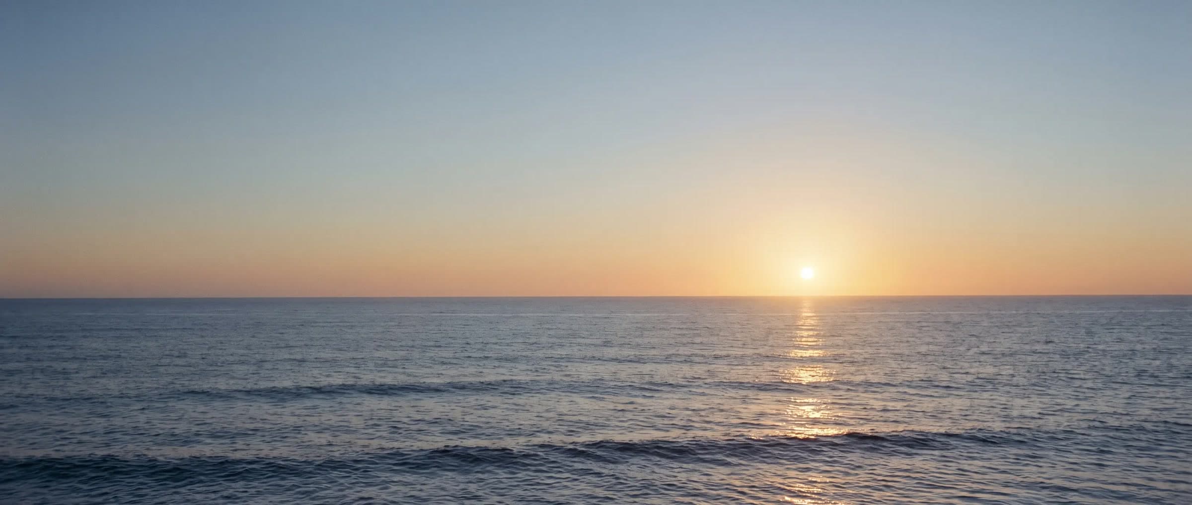 Open sea at sunset, the sun resting on the horizon, a path of gold on the water
