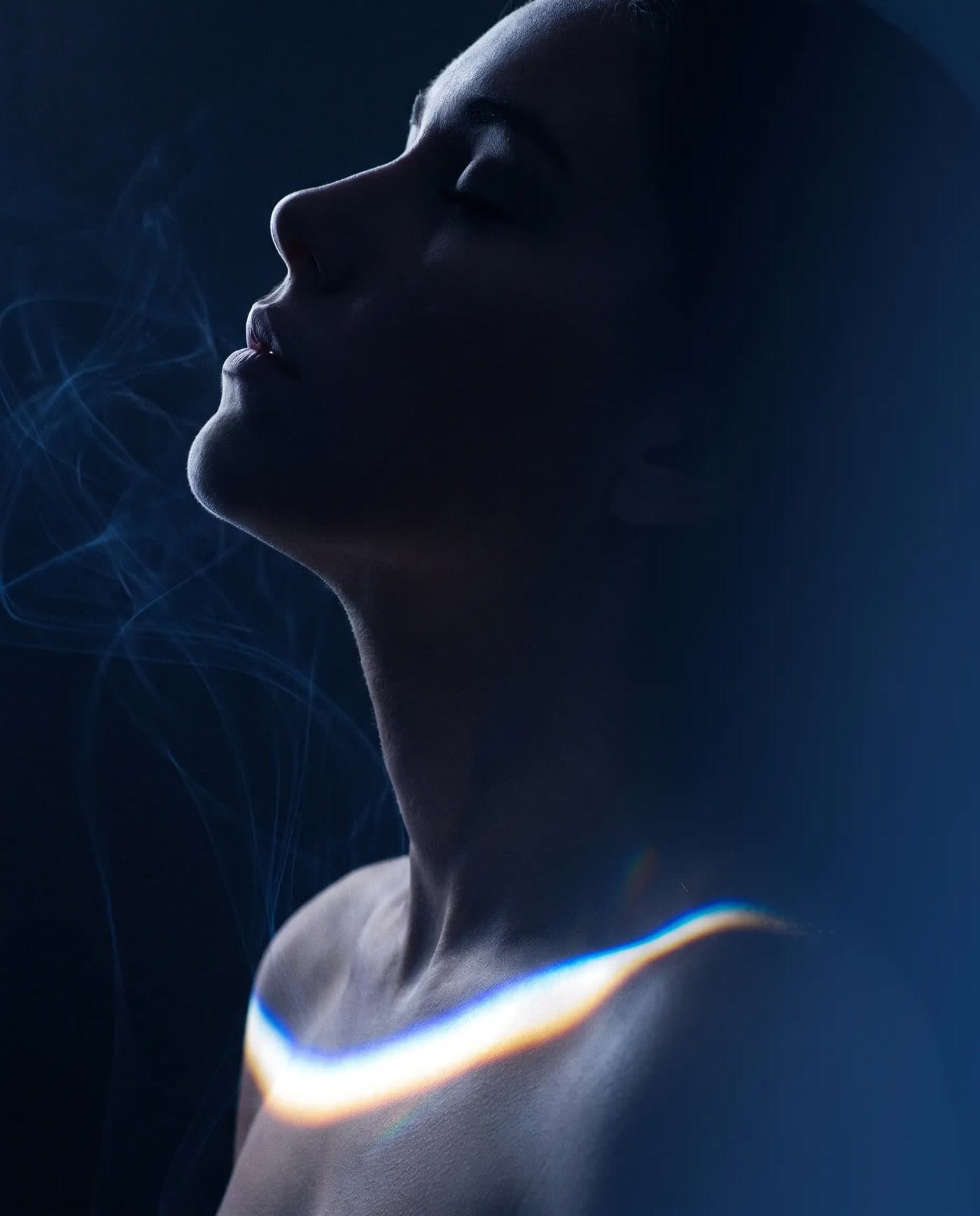 An anonymous figure in profile in deep blue, head tilted back, an arc of light across the collarbone